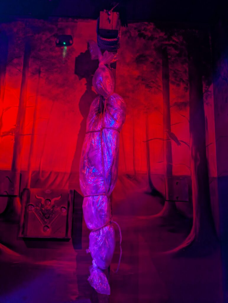 A prop of a human body folded in a plastic wrapping paper hanging from a wood on the neck